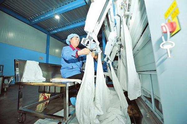 洗涤好的床品被挂上槽式烫平机自动拉展拽平